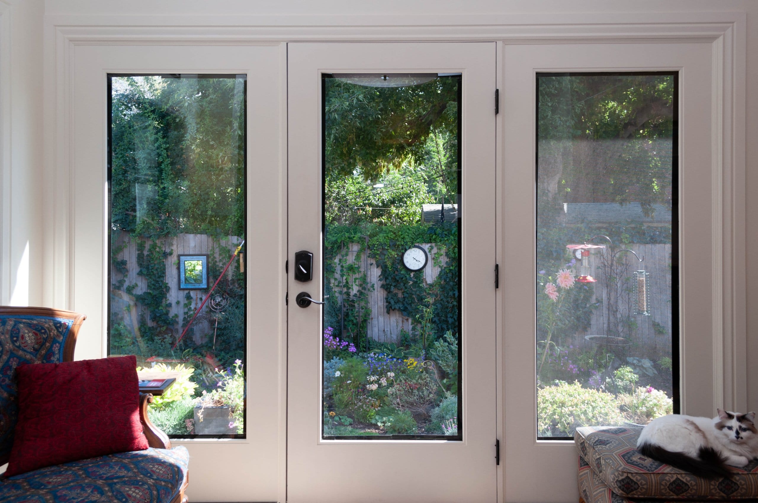 Glass doors and windows looking to the backyard. A cat sits on an ottoman to the right.