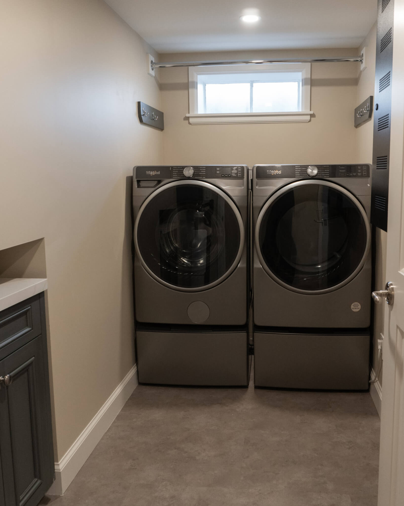 Side-by-side washer and dryer with a small window and rod to hang clothes on above.