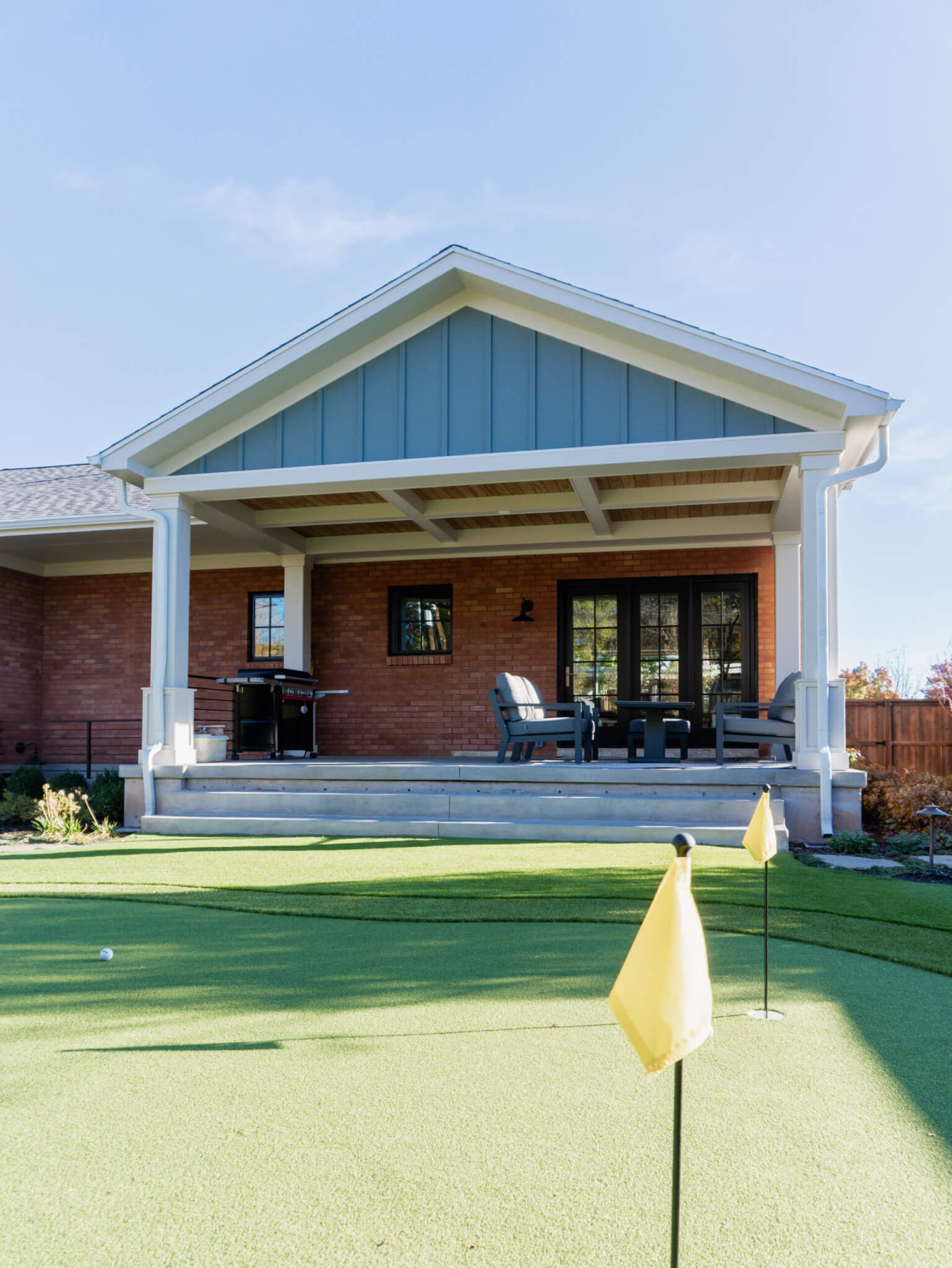 Backyard putting green and covered patio with seating and a grill.