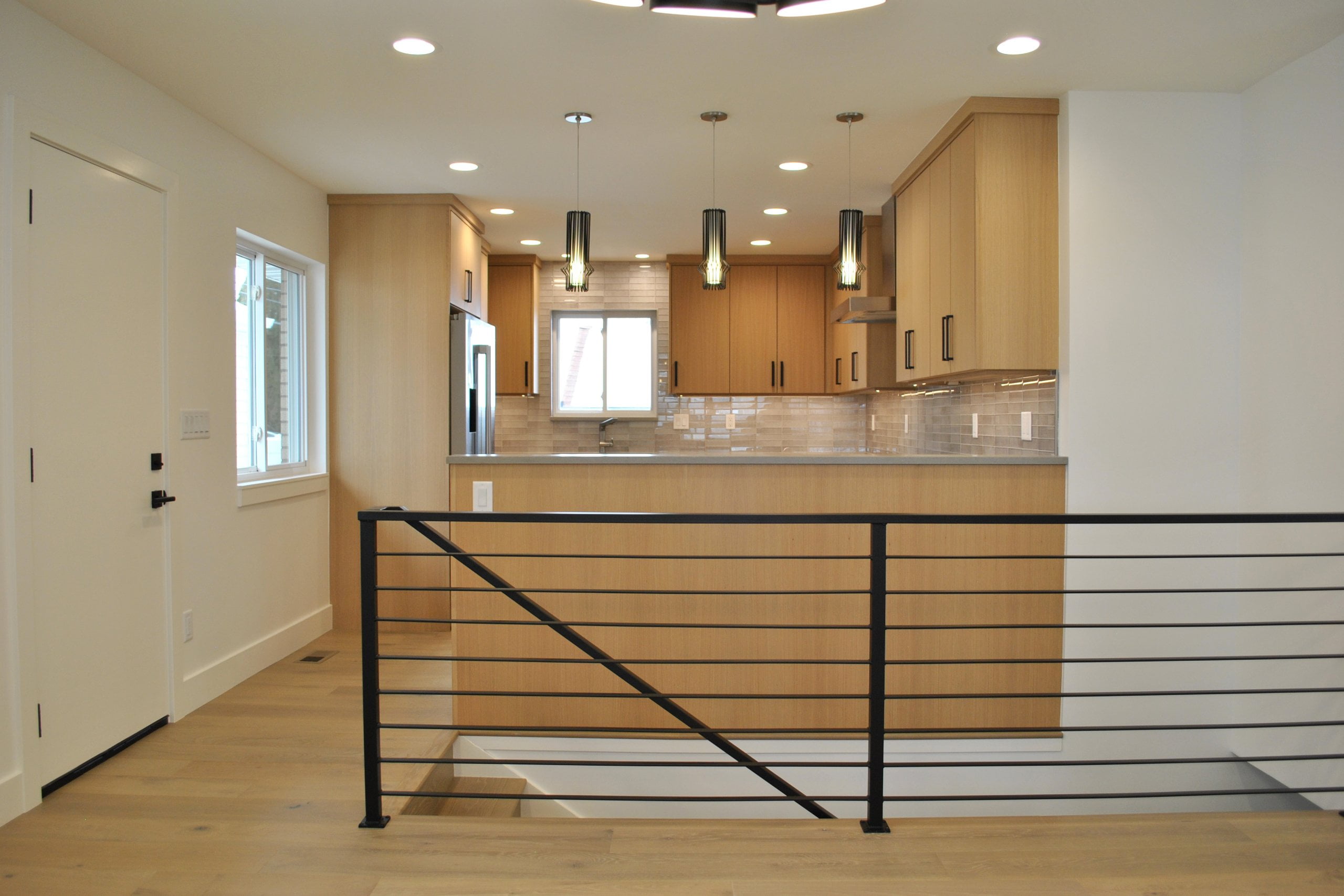 Modern staircase with door to the left and kitchen straight ahead behind a partial wall.