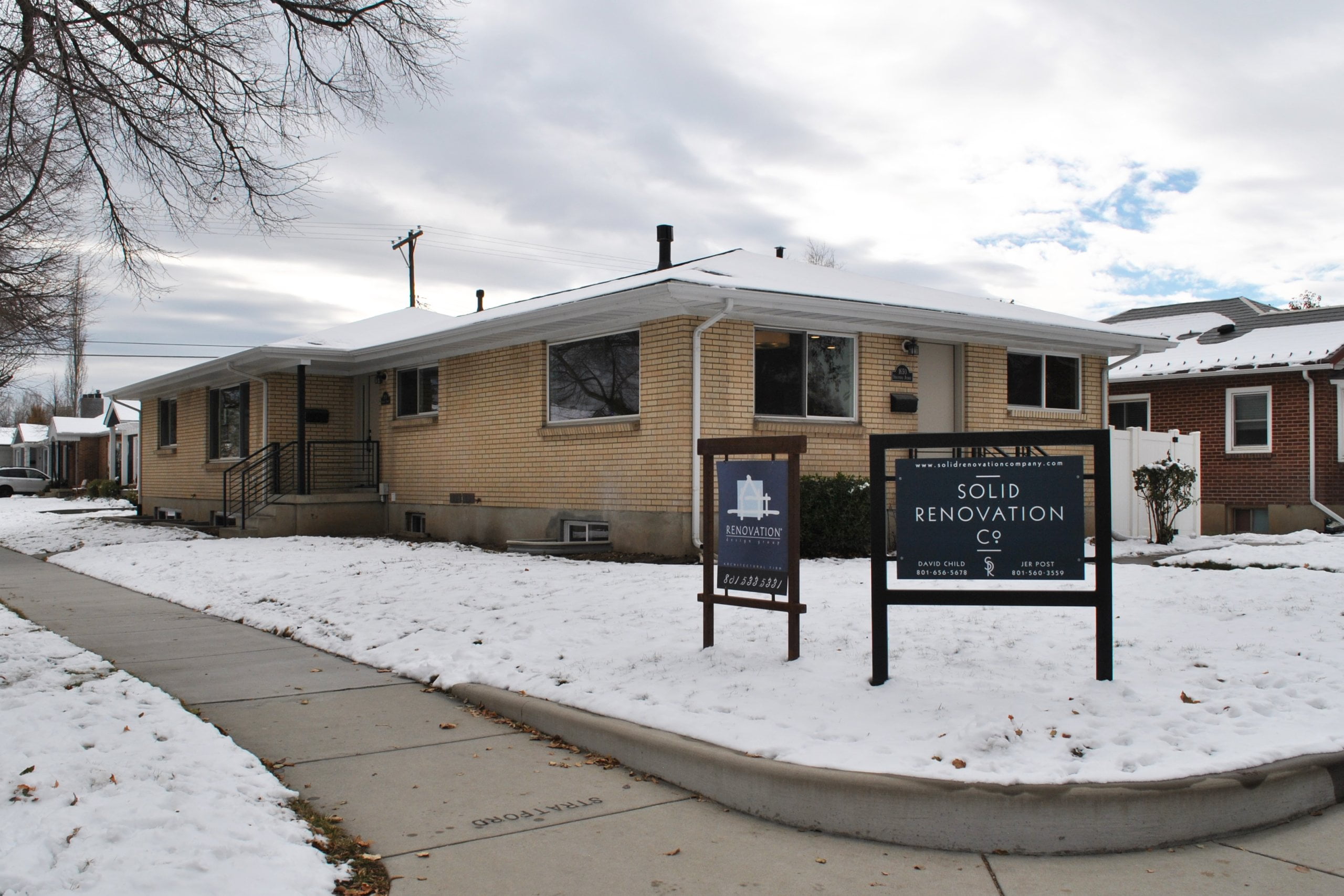 Exterior of duplex on a snowy day with two signs in the front yard. The first sign is for Renovation Design Group, and the second sign is for Solid Renovation Company.