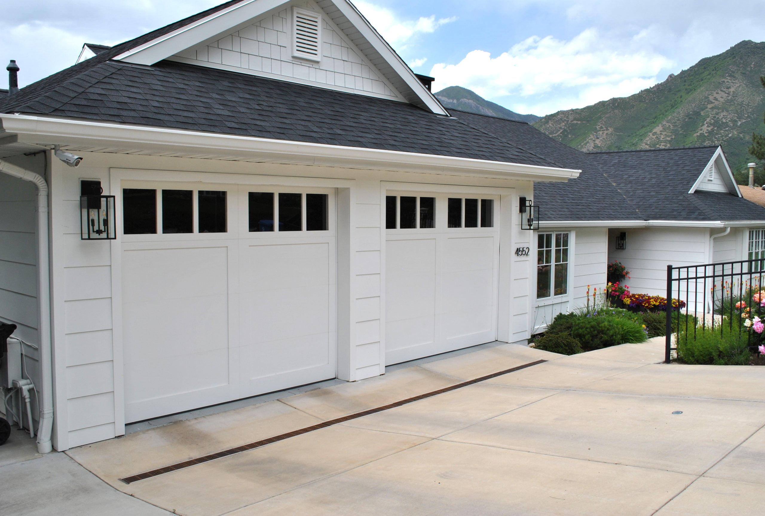 Exterior of house after the remodel. The house is located with a view of the mountains and includes two garage doors, flowers in the landscaping, and white siding and windows.