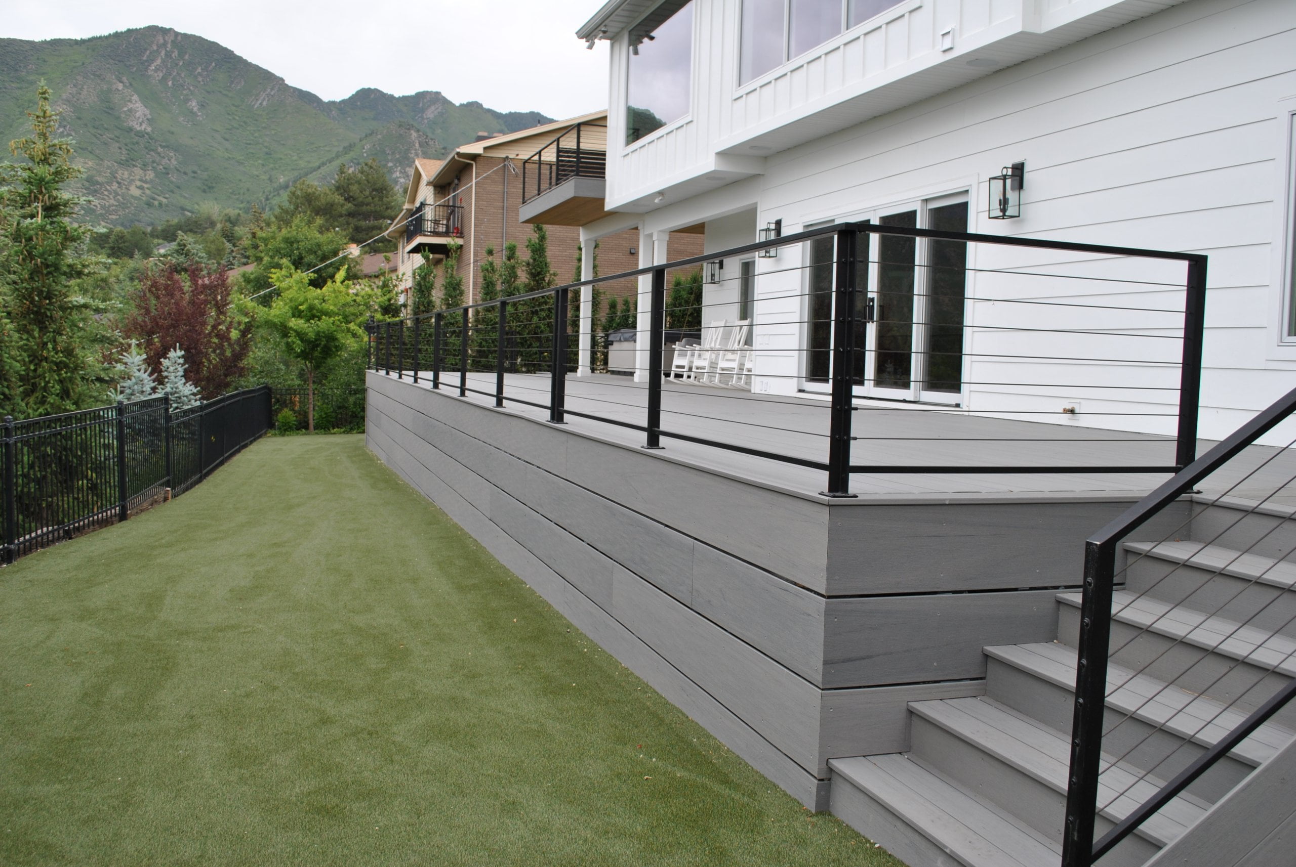 Large deck on the back of the house with a railing and stairs leading down to the turf.