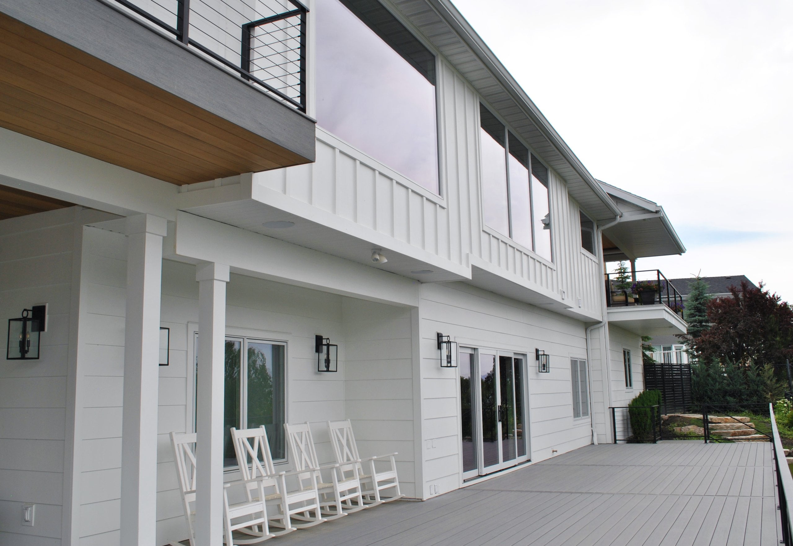 Large deck on the back of a home with additional decks above. Close to the house are four rocking chairs.