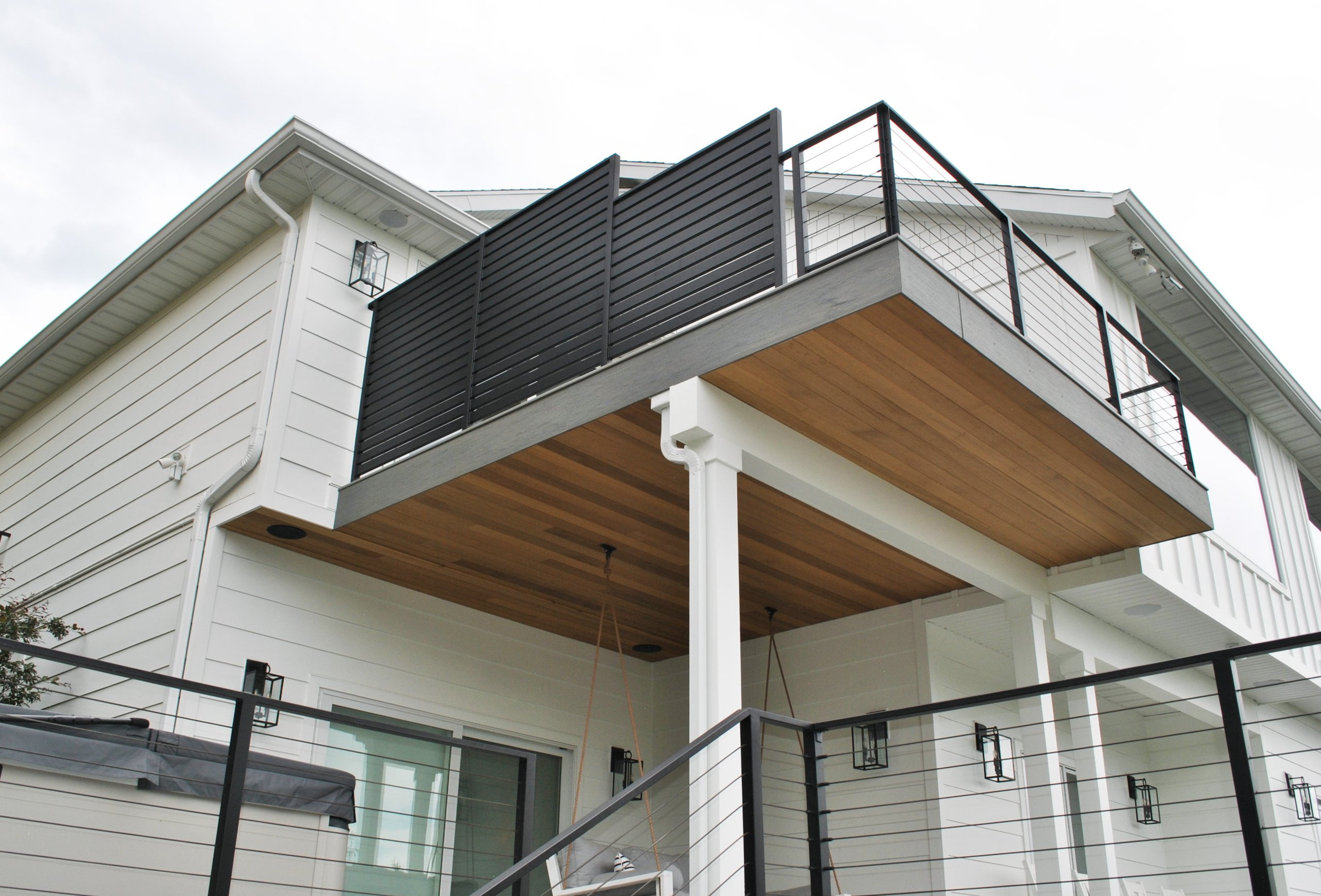 Two story deck with railing, hot tub, and porch swing.