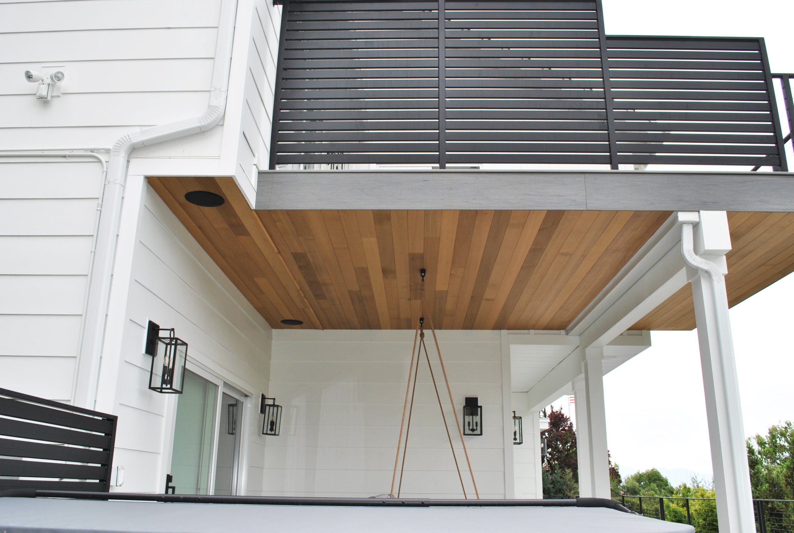 Two story deck with railing, hot tub, and porch swing.