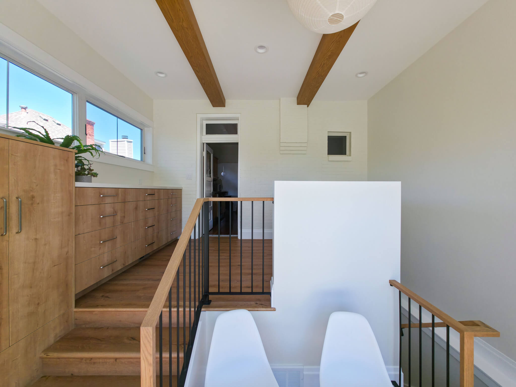 Large mudroom and laundry room addition with staircase. The space includes two chairs in a little alcove on the staircase landing and built-in cabinets along the exterior wall. Straight ahead is a brick wall with a door to the kitchen.