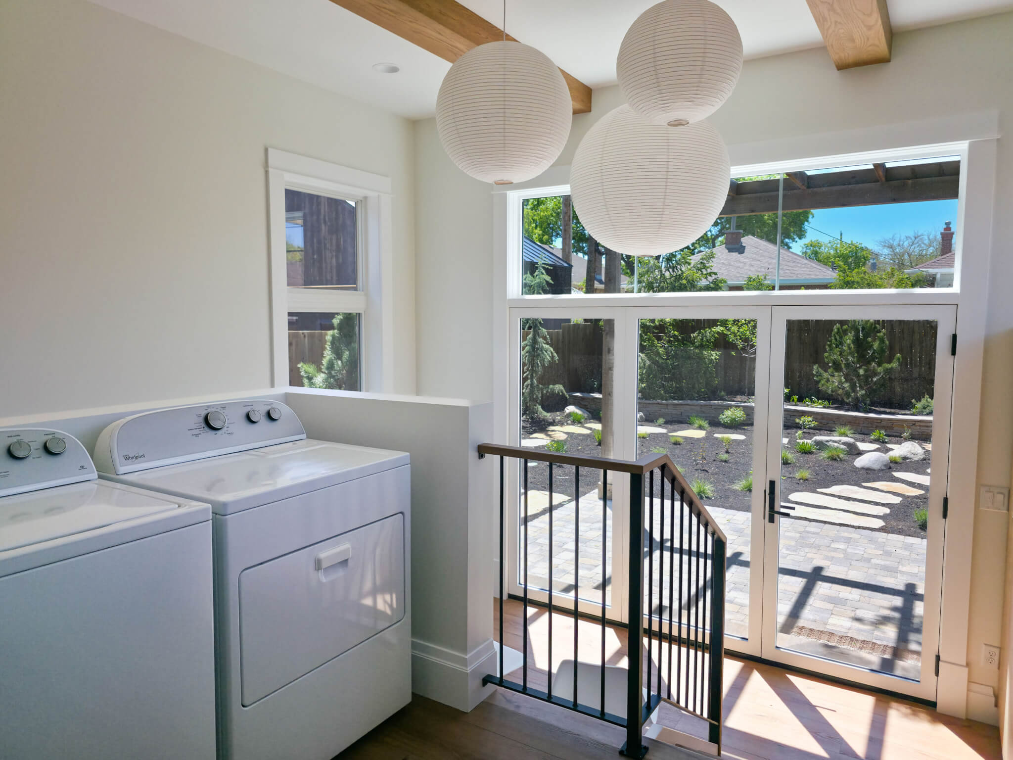 The laundry room section of the addition is located between the kitchen and mudroom. The space features lots of natural light, wood beams on the ceiling, and three round light fixtures.