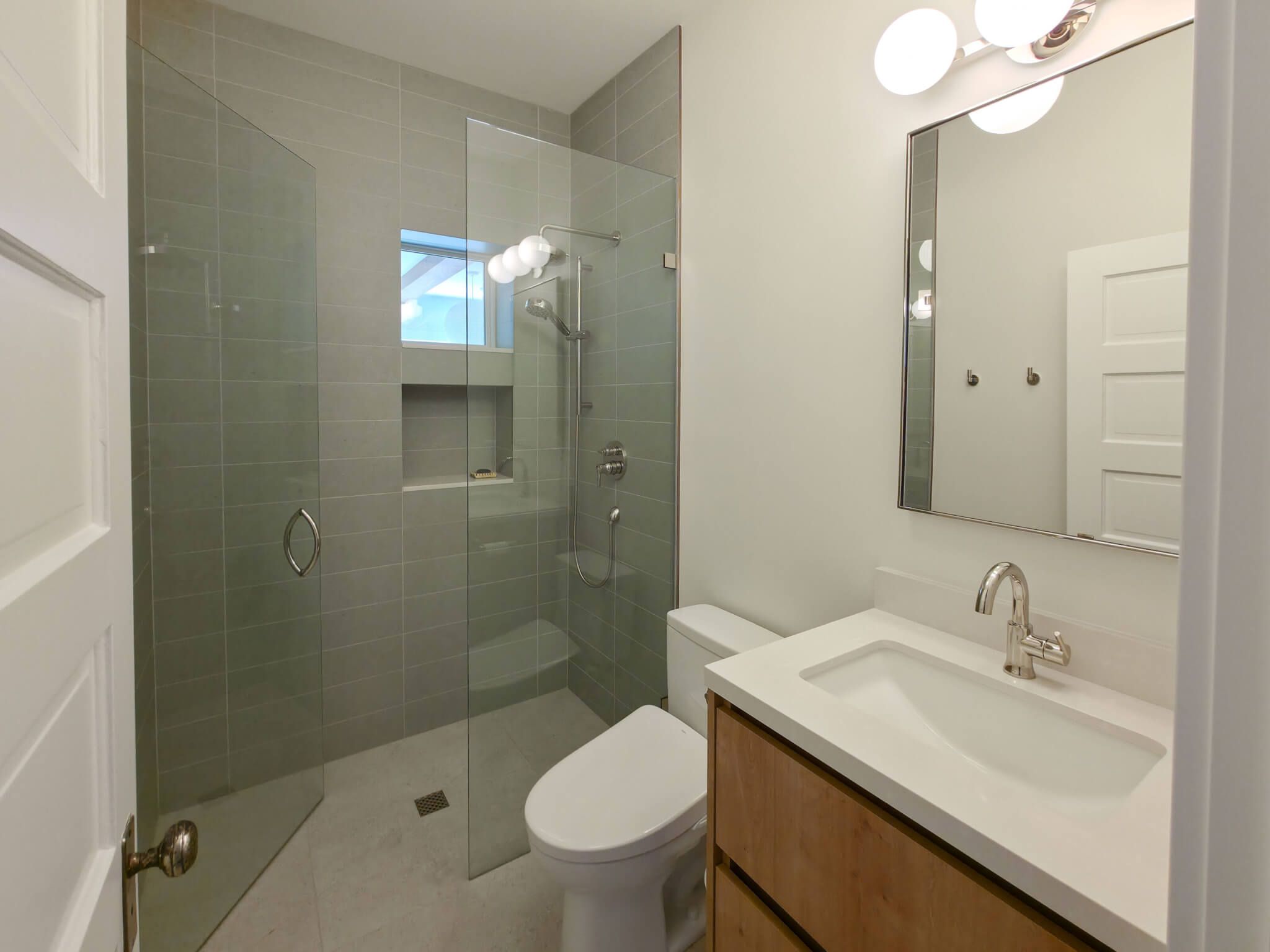 Bathroom remodel with a shower, toilet, and one sink vanity. The shower includes a niche for soaps and a small window.
