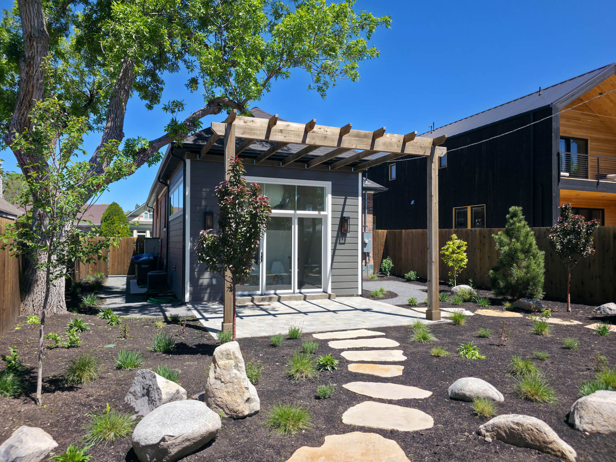 Exterior of the addition featuring new landscaping that includes various plants, a stone path, and a patio with a pergola.