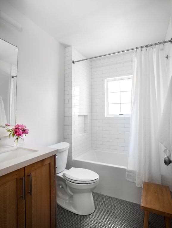 Bathroom design with wood vanity cabinet, white tile and window in the shower, and dark tile on the floor.