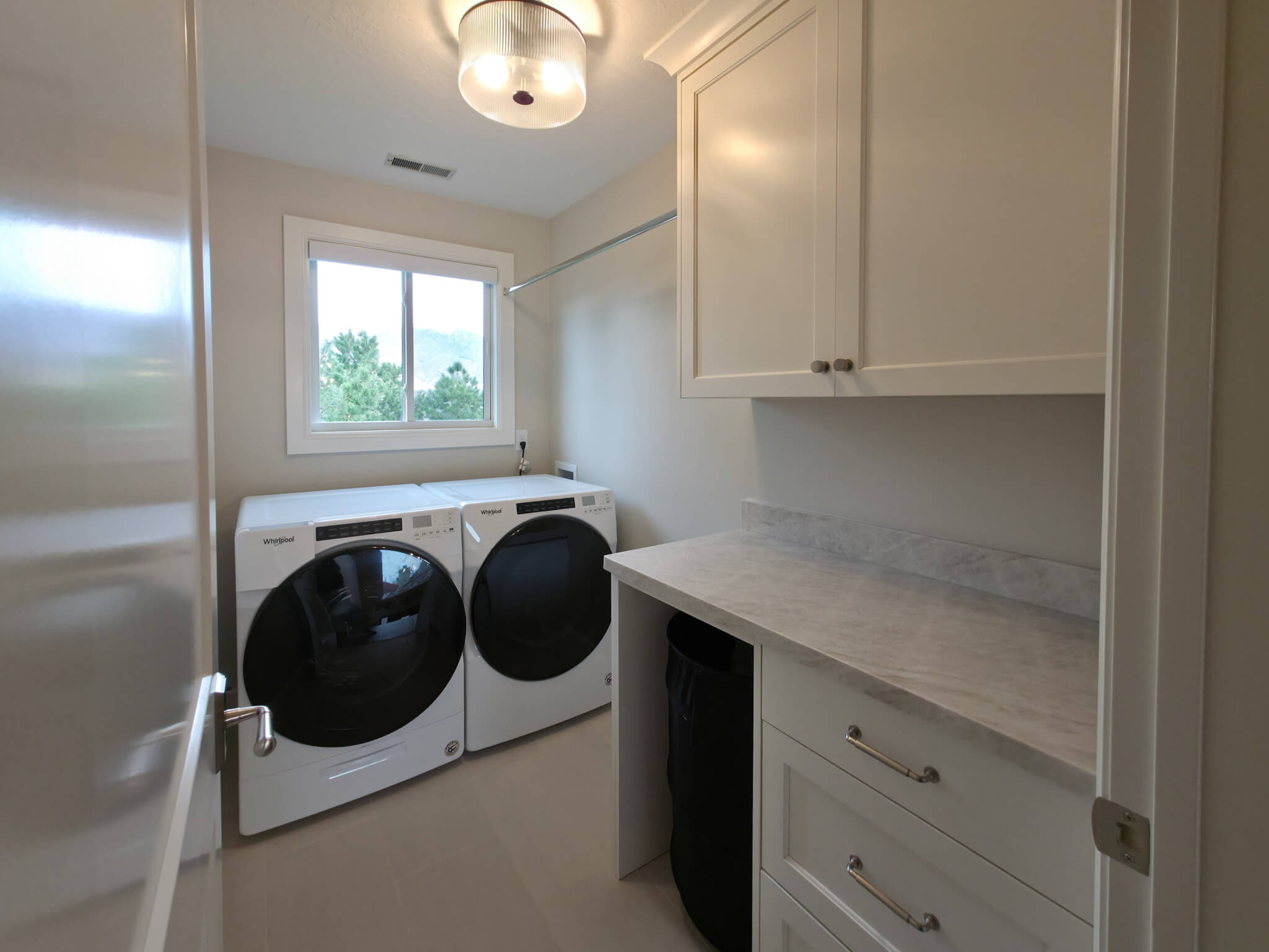 Laundry room with machines under the window and cabinets along the interior wall.