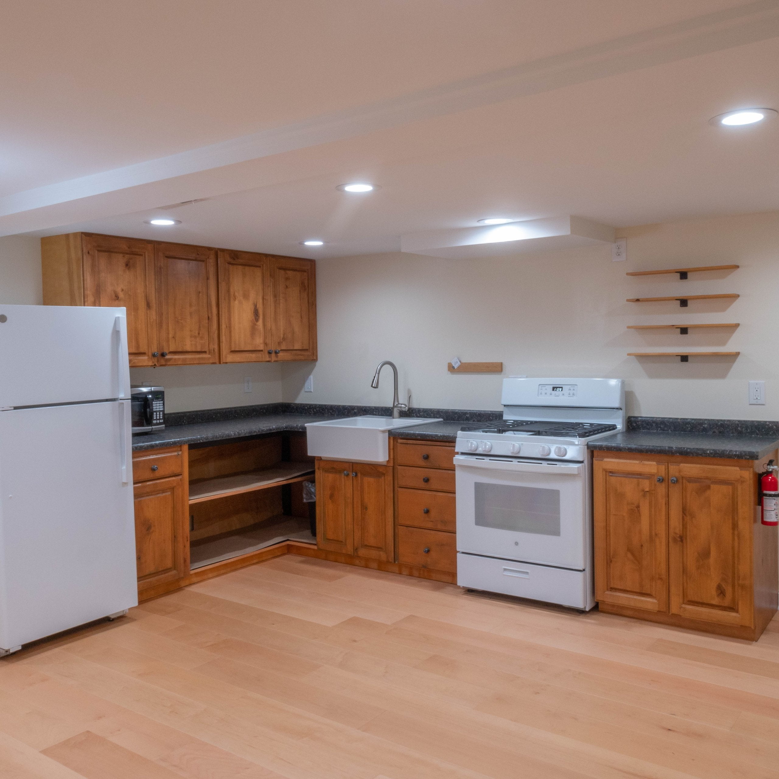 Basement apartment kitchen with wood cabinets, oven and stove, sink, and fridge.