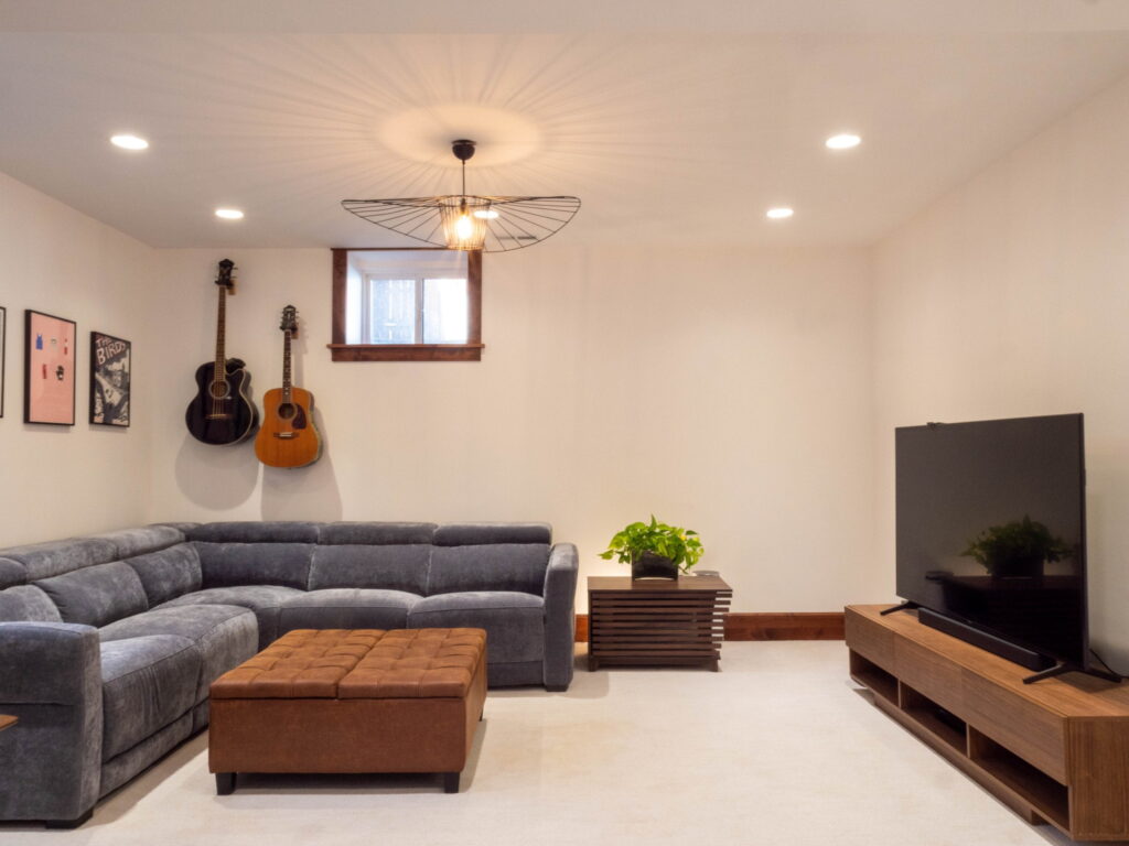 Basement family room couch with an ottoman in the center and a a tv to the right.