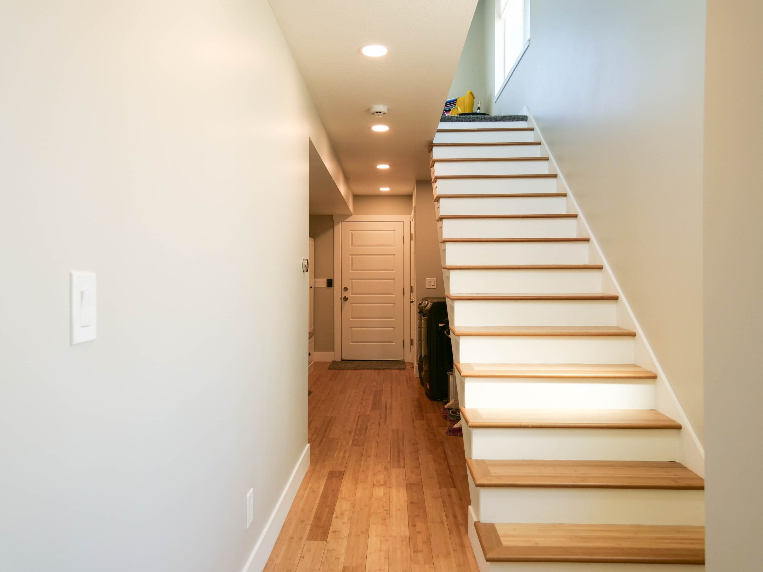 Hallway with a door at the end, laundry under the stairs, and an open staircase.