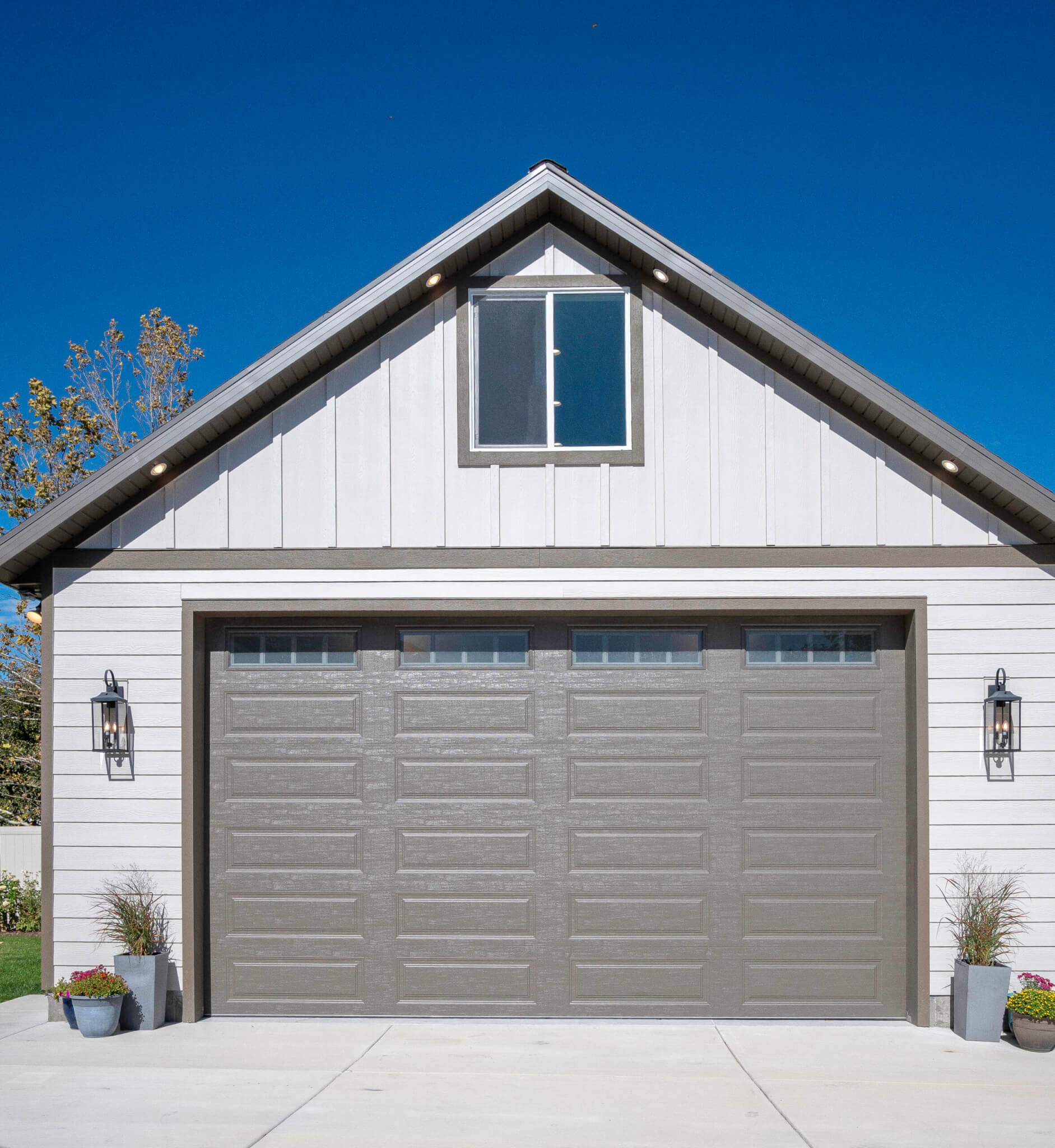 Front exterior of two-car garage door with a window above and lights hung on either side..