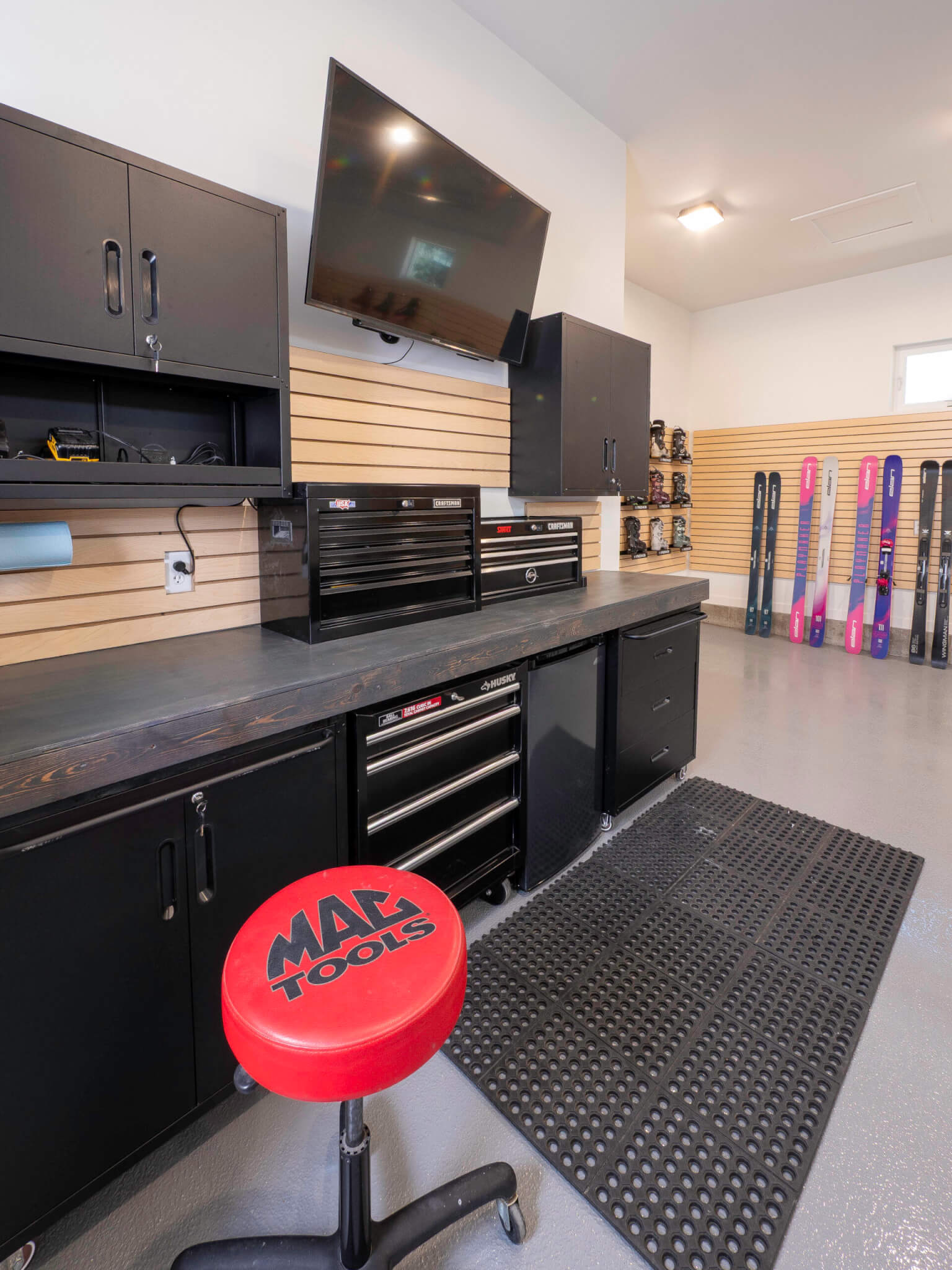 Workshop in the garage with built-in cabinets, a TV, and a rolling stool.