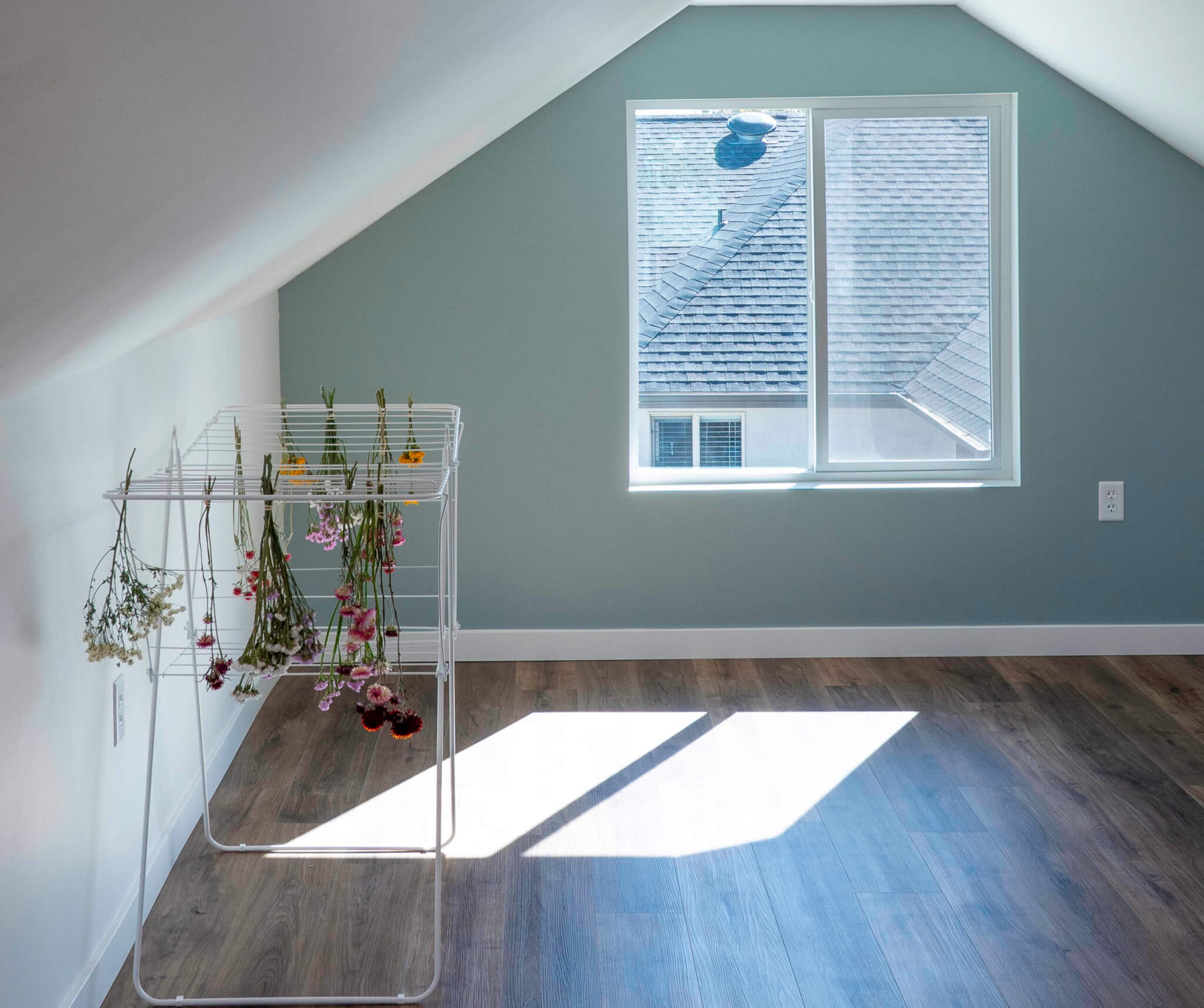 Finished garage attic with window and flowers drying on a rack along the wall.