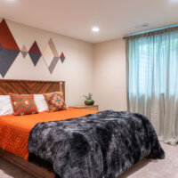 Thumbnail of http://Guest%20bedroom%20in%20the%20basement%20with%20curtains%20hung%20in%20front%20of%20the%20window%20and%20a%20bed%20positioned%20between%20two%20nightstands.