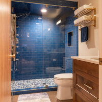 Thumbnail of http://Bathroom%20with%20blue%20tile%20in%20the%20shower,%20a%20toilet,%20and%20a%20vanity.