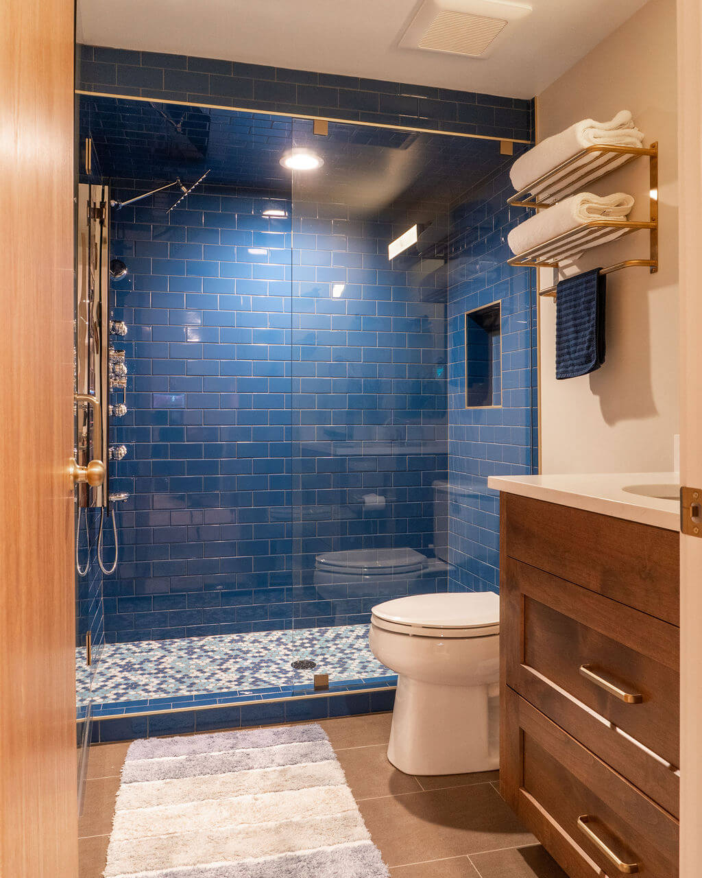 Bathroom with blue tile in the shower, a toilet, and a vanity.
