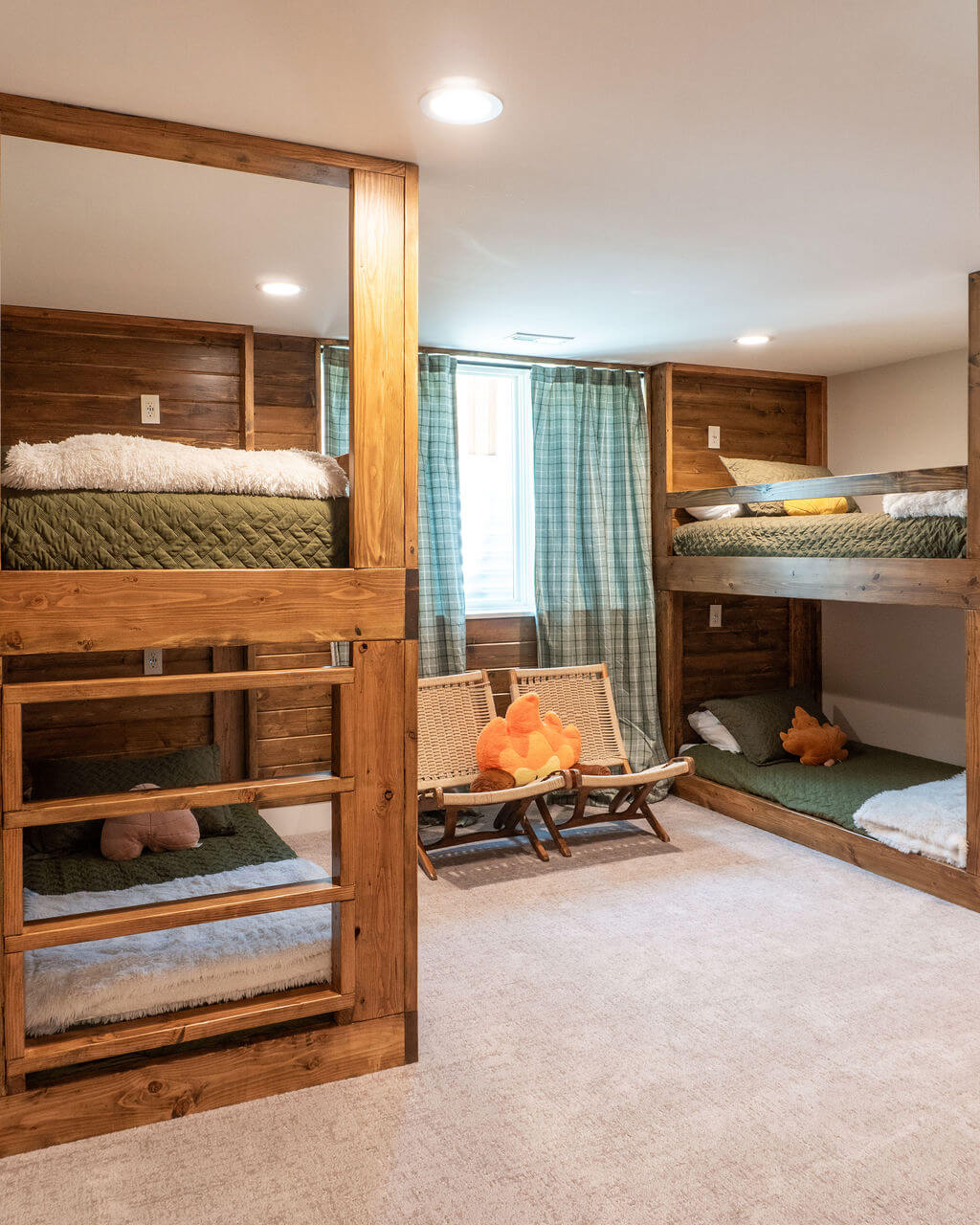 Basement bunk room with two sets of built-in bunks for a total of four beds and two chairs in front of the window.