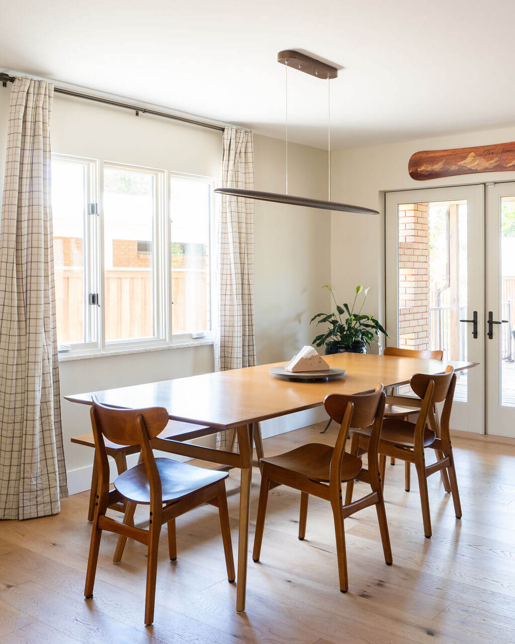 Dining room with natural light from the window and door to the deck, a modern light fixture, and wood table with seating for six.