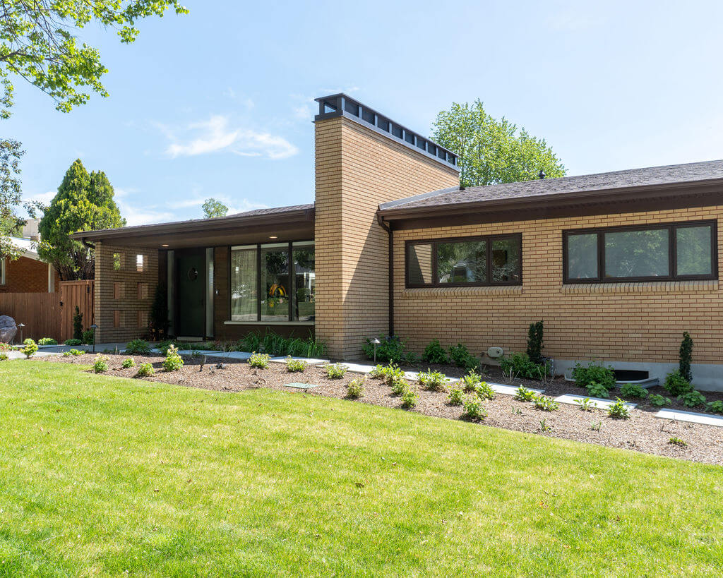 Mid-century exterior of a brick home with a large chimney, front porch, and updated landscaping.