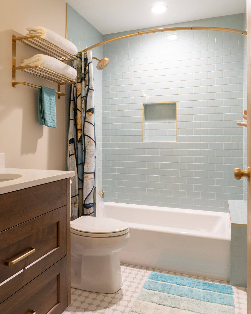 Guest bathroom with a tub and shower combination, toilet, and vanity. The design features a light blue tile and gold fixtures.