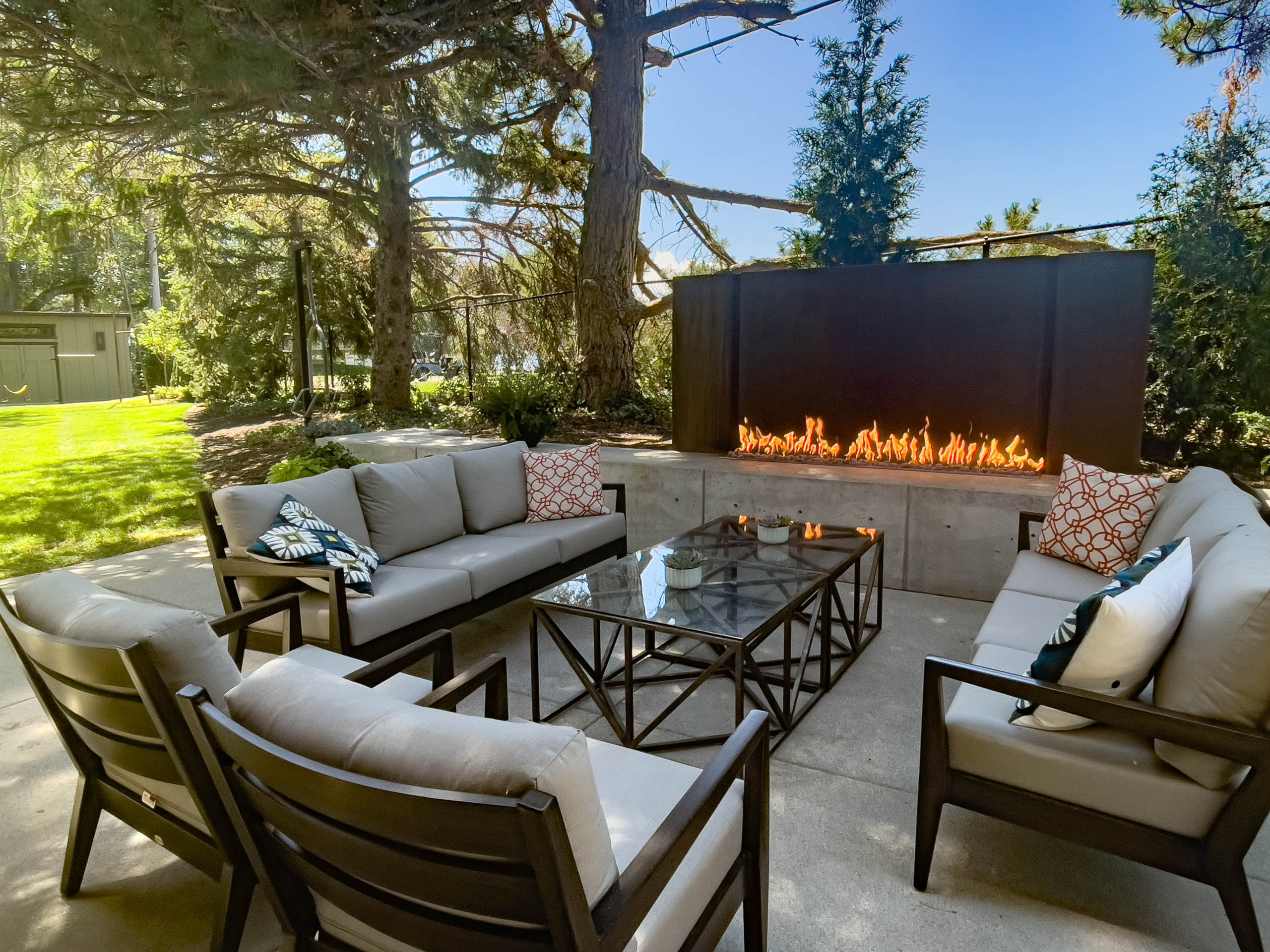 Outdoor fireplace with two couches, chairs, and a coffee table in front.