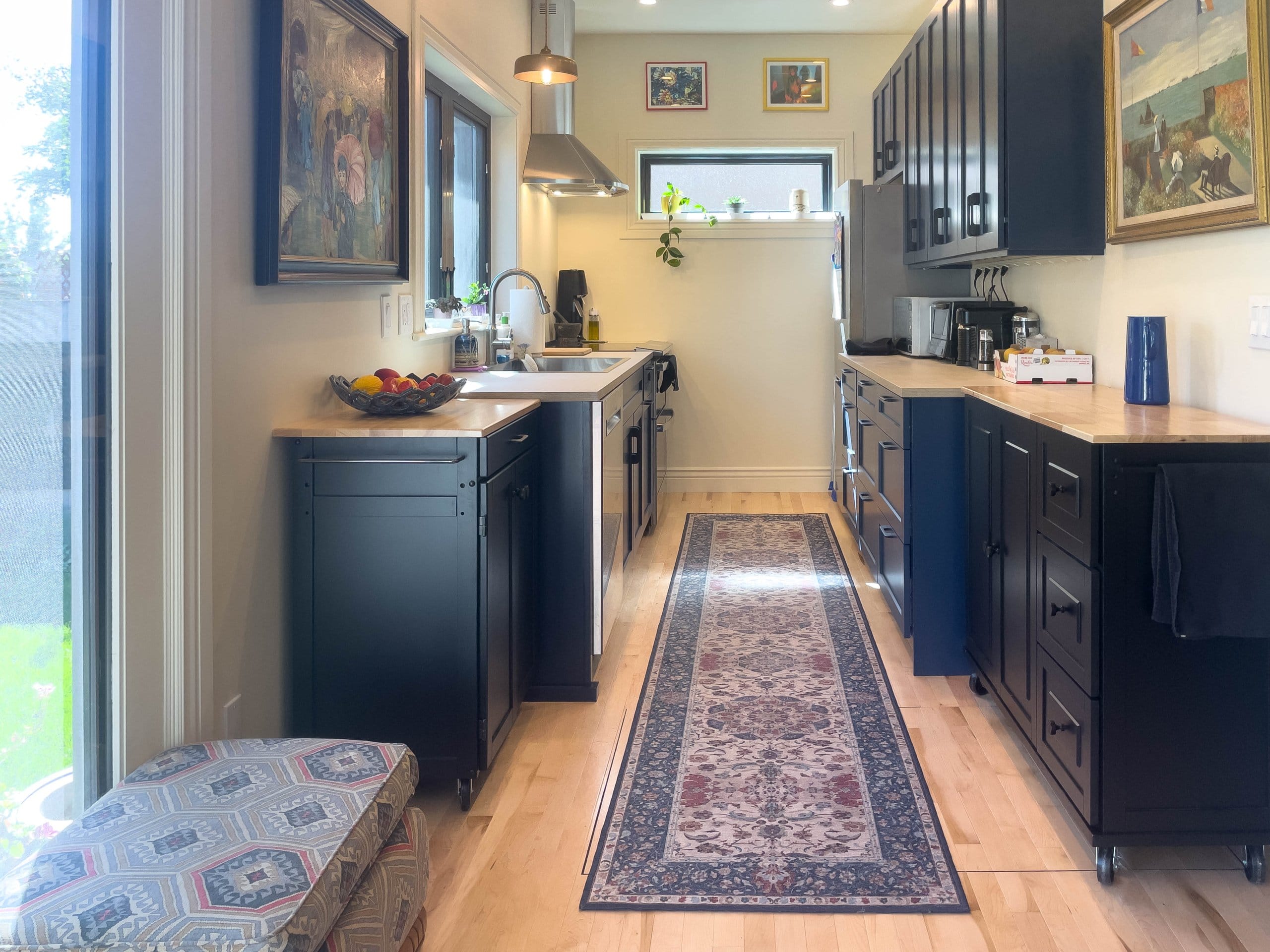 Kitchen addition in a galley layout with blue cabinetry, rug down the center, windows, and two rolling carts for additional storage and prep space.