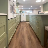 Thumbnail of http://Large%20kitchen%20with%20green%20cabinets,%20gold%20hardware,%20and%20white%20appliances.%20In%20the%20middle%20is%20a%20large%20island%20with%20seating%20and%20lights%20hung%20above.