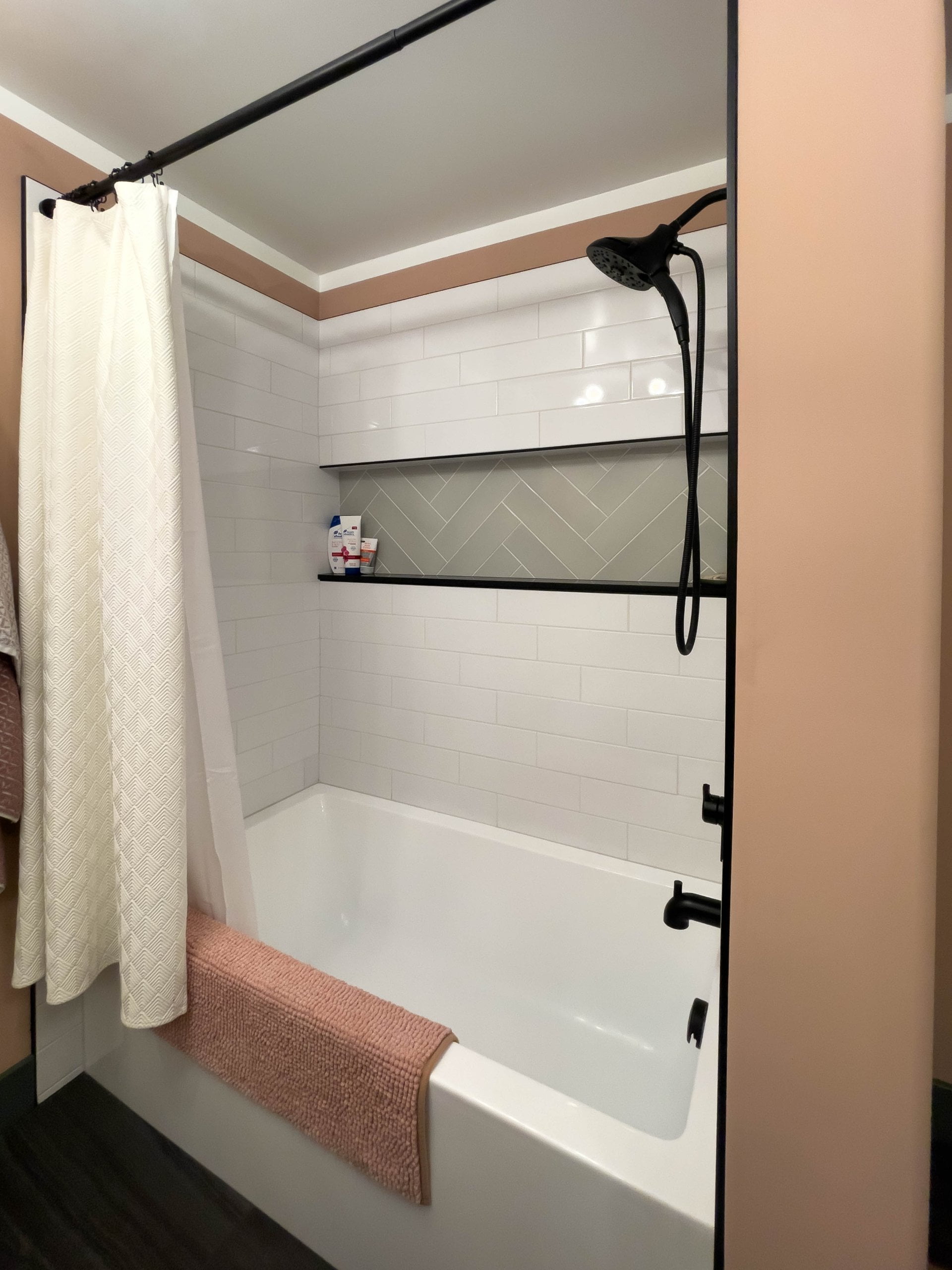Shower and tub combination with a niche, shower rod and curtain, and detachable shower head. A pink bath mat is hung along the edge of the tub.