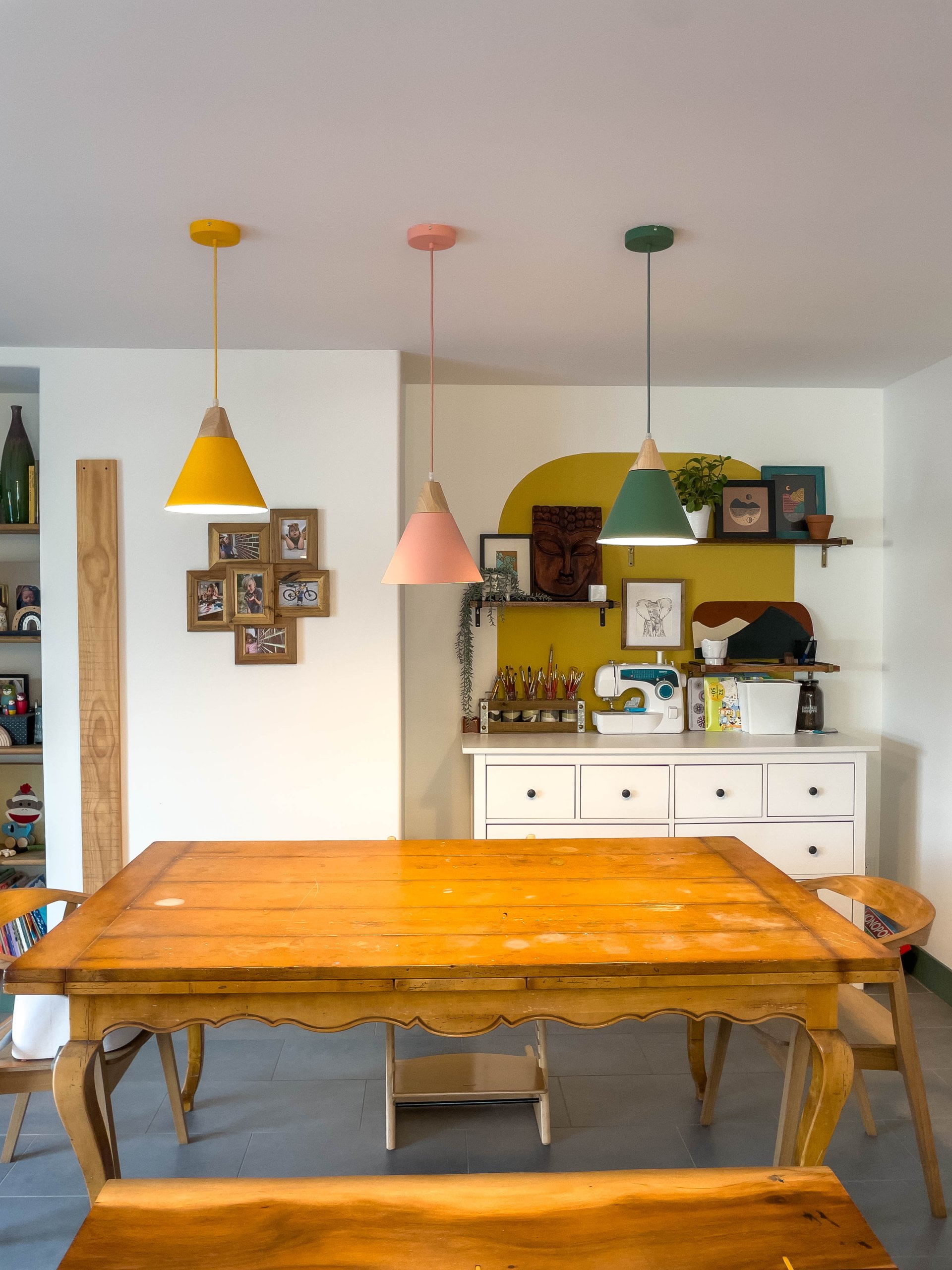 Wood table with three lights hung above and a dresser for crafts behind.