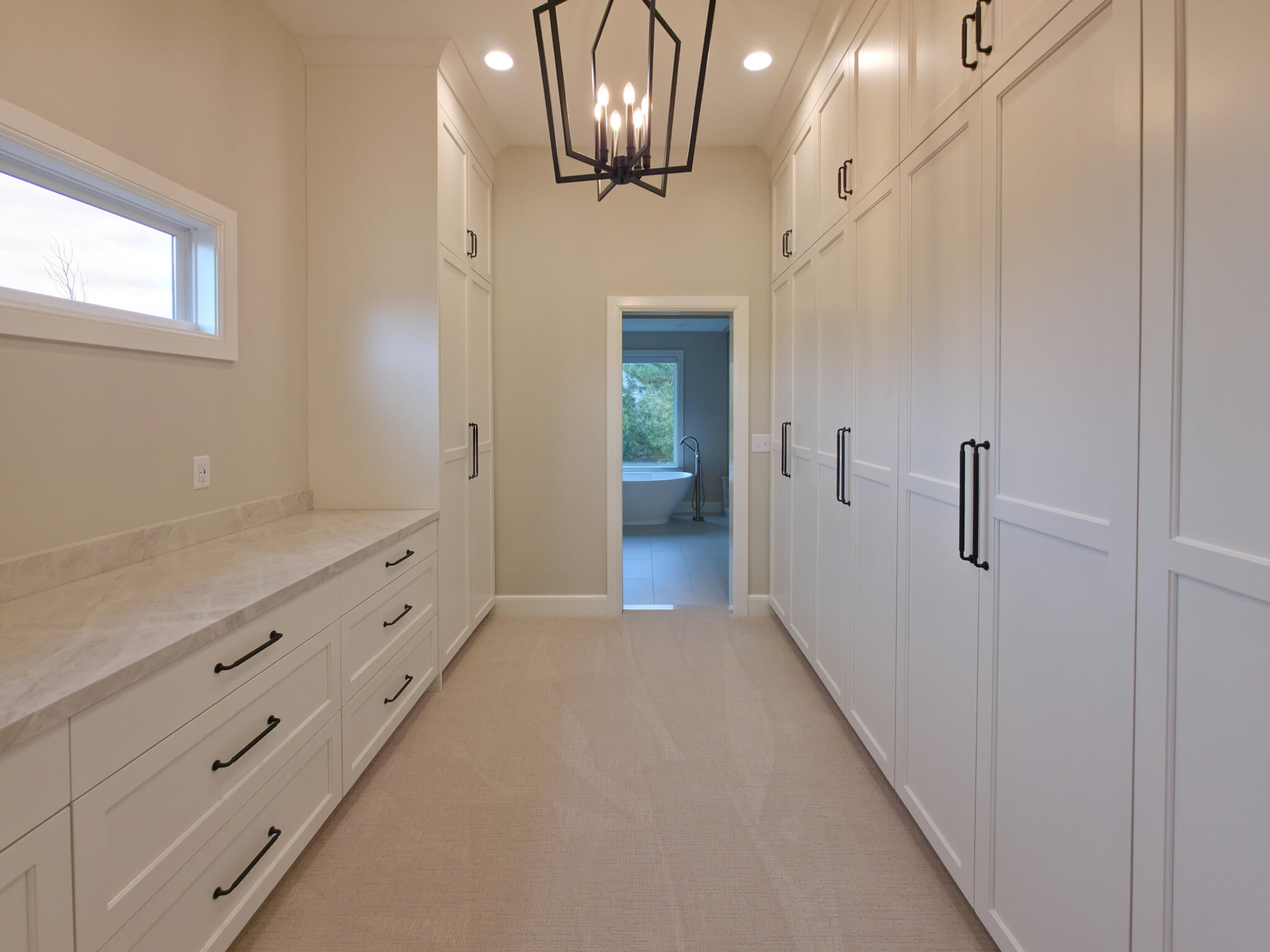 Large walk-through closet with white cabinets, carpet, and a chandelier above.