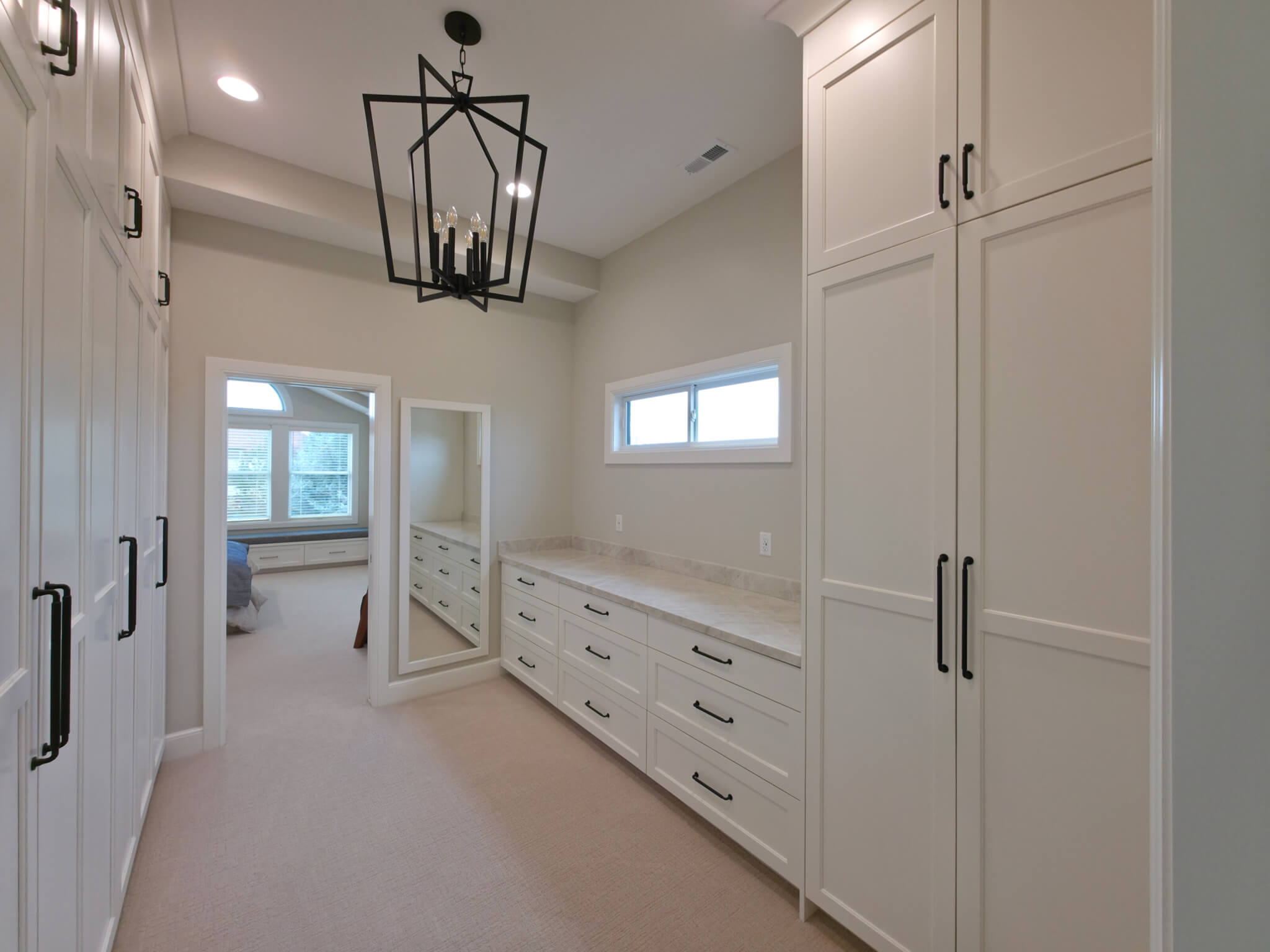 Large walk-through closet with white cabinets, carpet, and a chandelier above.