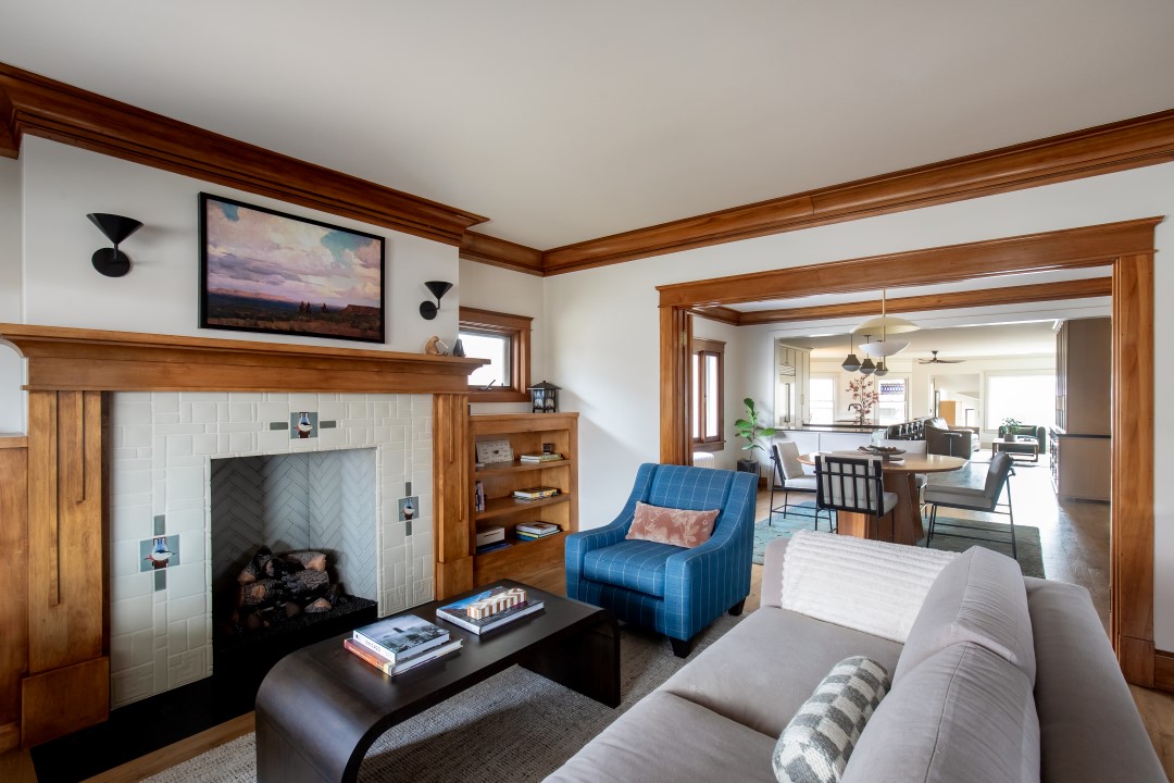 Historic home living room with wood details in the trim, casing, and built-in bookshelves on either side of the fireplace. The entire room is open to the dining room through a cased opening, and the fireplace serves as a focal point with a beautiful tile surround.