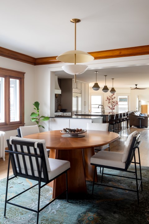Historic home dining room with wood trim details, oval table with seating for four and pendant light above, and opening with view to the kitchen.