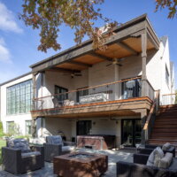 Thumbnail of http://Backyard%20and%20outdoor%20entertaining%20space%20at%20a%20house.%20The%20lower%20level%20includes%20a%20partially%20covered%20patio%20with%20a%20hot%20tub%20and%20furniture%20around%20a%20fire%20pit.%20Upstairs,%20a%20covered%20deck%20includes%20ceiling%20fans,%20outdoor%20furniture,%20and%20a%20modern%20railing.%20Both%20levels%20have%20doors%20to%20the%20interior%20and%20are%20connected%20by%20a%20staircase%20on%20the%20right%20side.