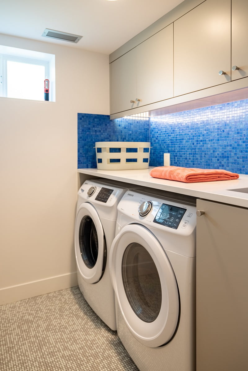 Basement laundry room with a small window, blue tile backsplash, and side by side washer and dryer tucked under the counter.