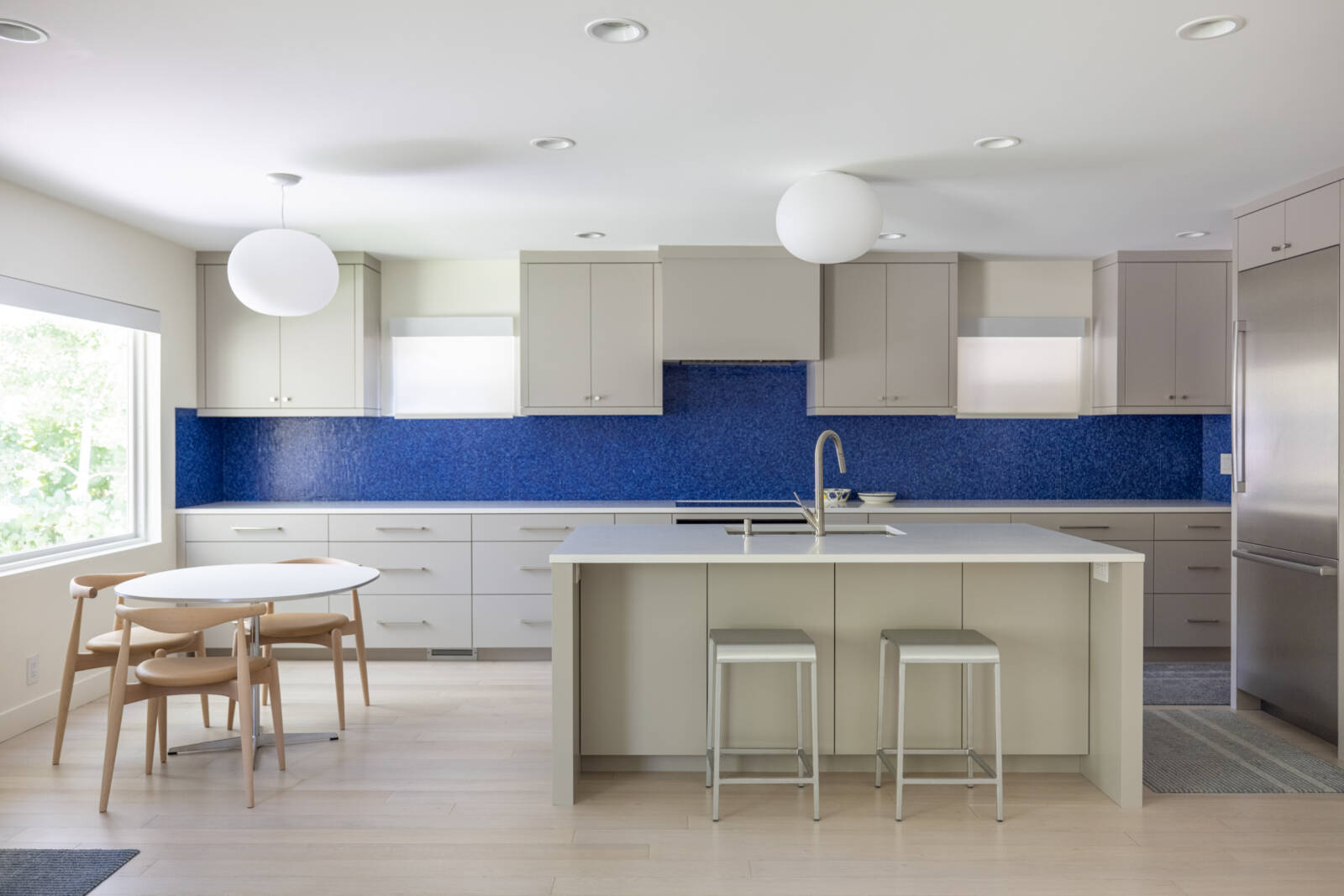 Modern kitchen renovation that is open to the dining room and has an island, blue tile backsplash, and lots of natural light.