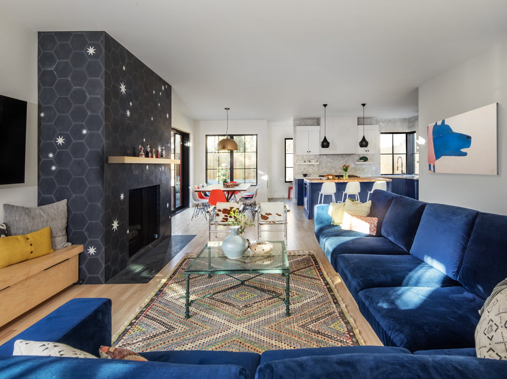 Open concept living room with a view to the dining room and kitchen. In the living room is a large blue couch, two chairs, and a fireplace.
