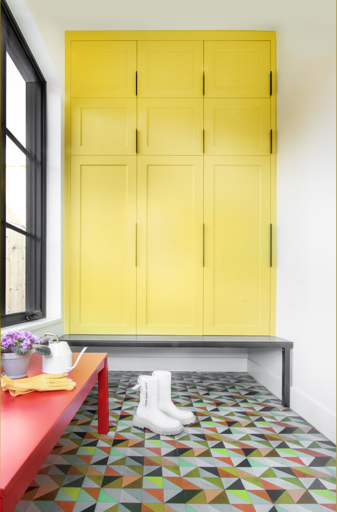 Mudroom with colorful tile on the floor, a red bench, and yellow cabinets.