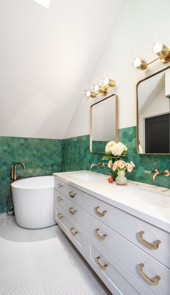Primary bathroom with double vanity and soaking tub. The design finishes include green hexagon tiles on the wall, white hexagon tiles on the floor, and gold fixtures.