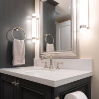 Thumbnail of http://Bathroom%20vanity%20with%20storage%20below,%20a%20towel%20hung%20to%20the%20side,%20and%20a%20mirror%20framed%20by%20two%20lights%20above.