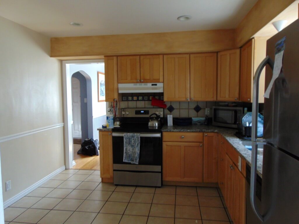 Kitchen before the renovation with tile flooring, wood cabinets, and a stove along the wall with an opening to the dining room.