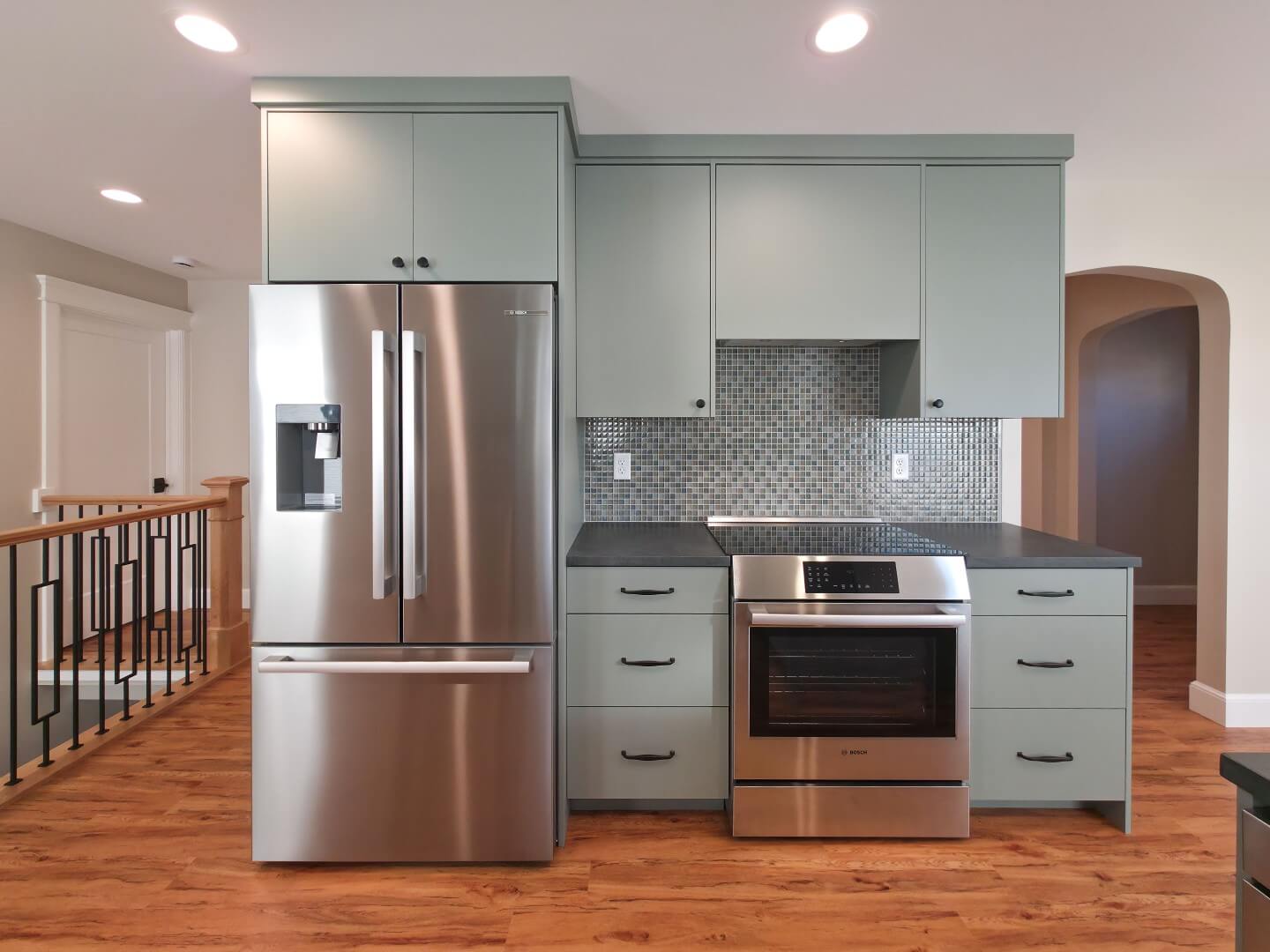 The fridge, cabinetry, and the stove and oven along an interior wall. On the left is an opening with the staircase, and on the right is the dining room with an archway leading to the living room.