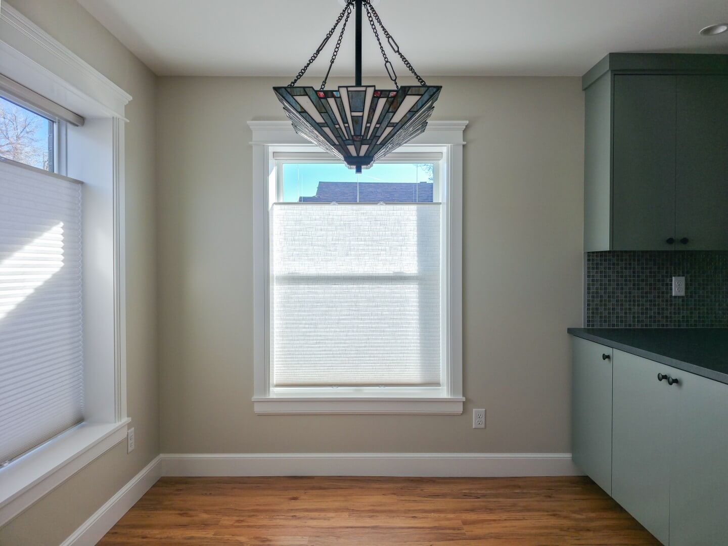 Updated dining room with the kitchen to the right, a light hanging from the ceiling in the center, and two windows.