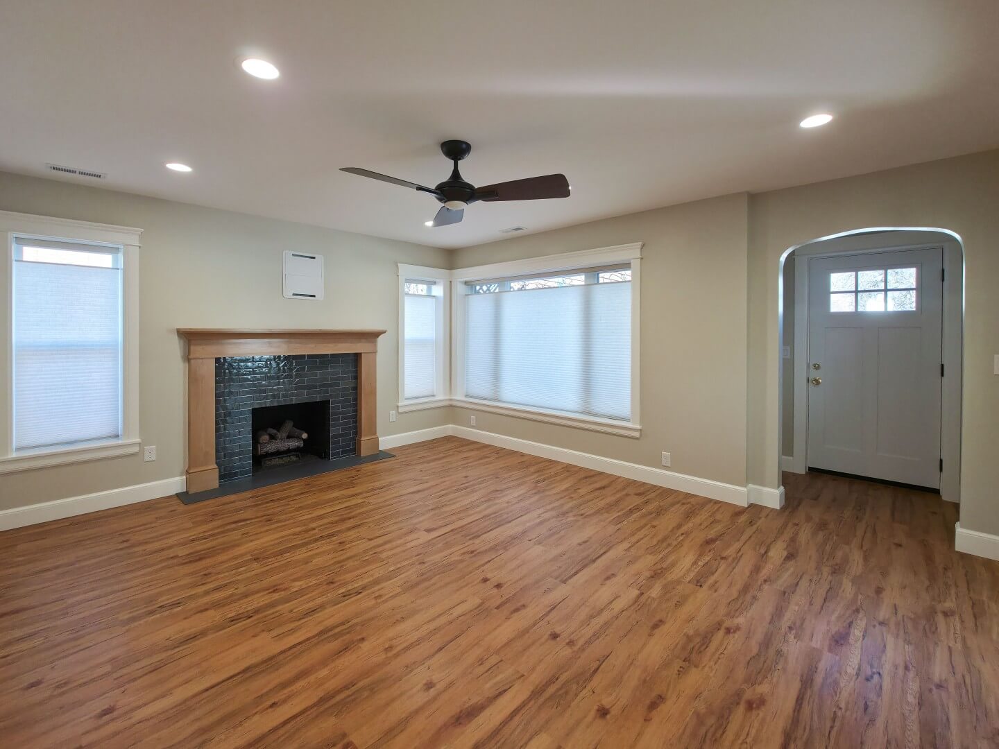 Renovated living room with a ceiling fan, updated fireplace, wood flooring, and multiple windows.