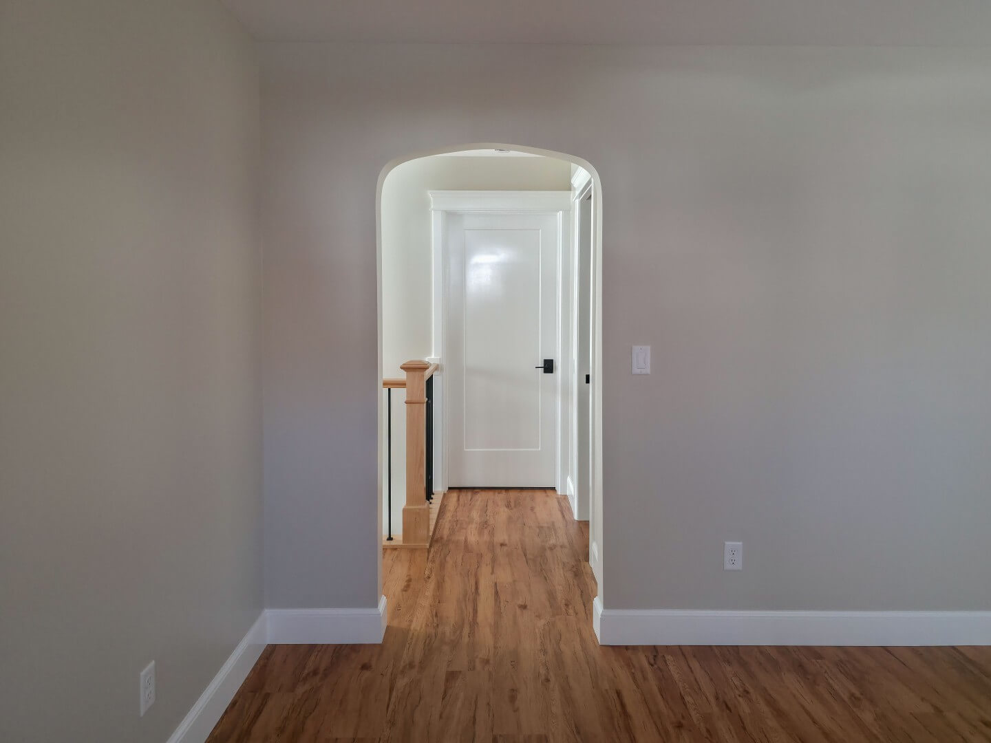 Archway looking from the living room to the hallway. The hallway includes the staircase railing and closed doors leading to the primary suite and powder bathroom.